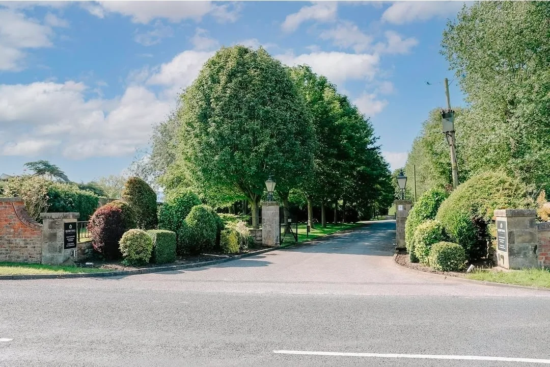 The tree-lined entrance to the estate between stone gateposts.