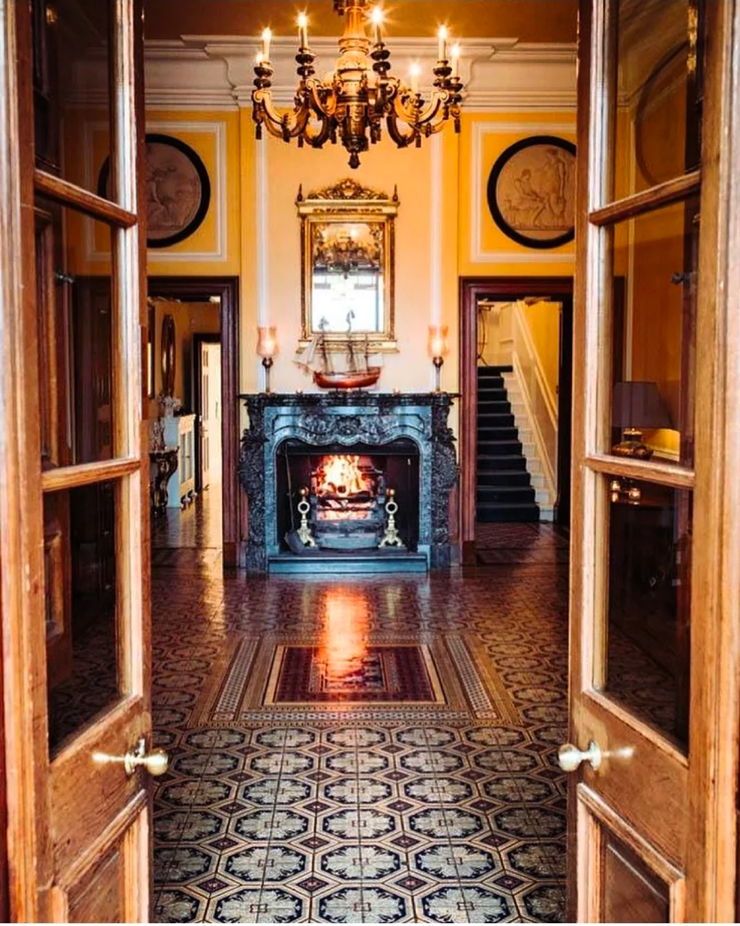 A view through an ornate hallway towards a fireplace and chandelier.